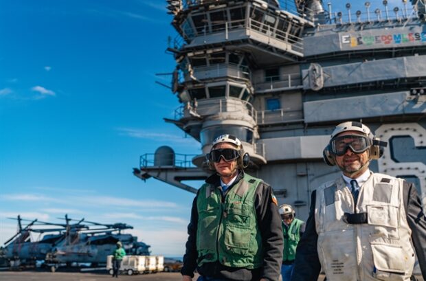 Presidente Kast y el canciller Pérez-Mackenna usando cascos, gafas protectoras y chalecos de seguridad (uno verde y otro beige), posan en la cubierta de vuelo de un portaaviones.