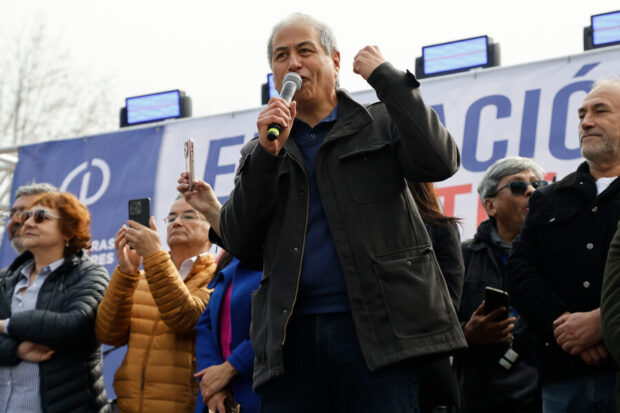 El presidente del Colegio de Profesores, Mario Aguilar, realiza un discurso. A su espalda se observan docentes y un escenario con luces.