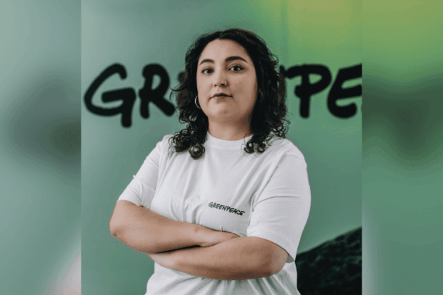 Retrato de la abogada y encargada de Incidencia de Greenpeace, Roxana Núñez. Usa una popera blanca y atrás de ella se ve en grande en una pared verde y con letras negras "Greenpeace".