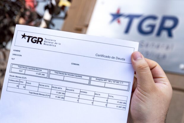 Mano sostiene certificado de deuda de la Tesorería General de la República. Atrás se ve borroso el logo de dicho organismo.
