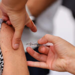 Manos inyectando una vacuna en un brazo.