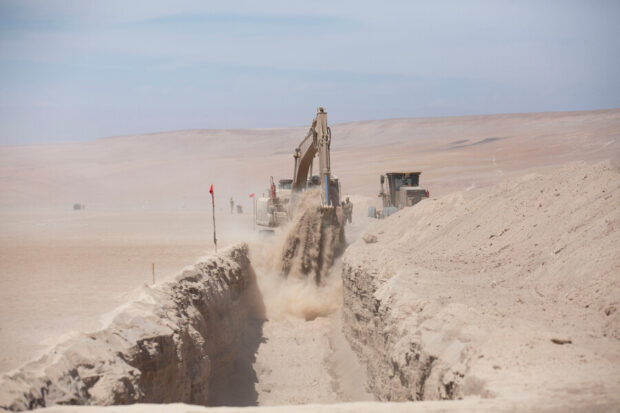 Maquinaria pesada excavando una zanja en medio del desierto en la frontera norte de Chile bajo un cielo despejado.
