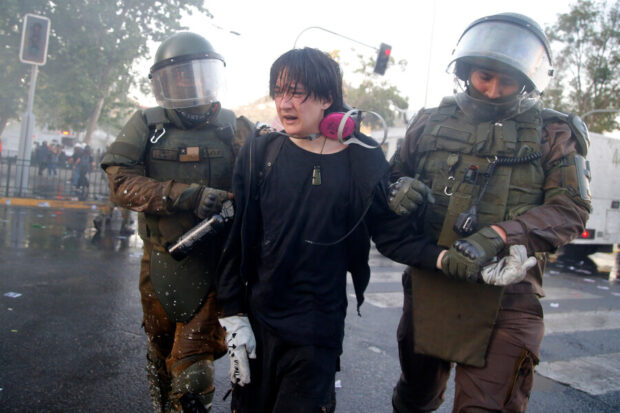 Carabineros detienen a una joven en el marco de las manifestaciones por el quinto aniversario del estallido social.