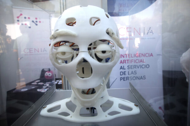 Un prototipo de cabeza robótica de color blanco, con estructura abierta que deja ver sensores, cables y mecanismos internos, exhibida dentro de una vitrina.
