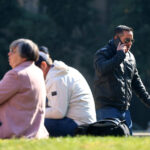 Adultos mayores sentados en un parque y un hombre hablando por teléfono mientras camina.