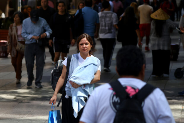Mujer camina con su bebé en brazos y una bolsa de compras.