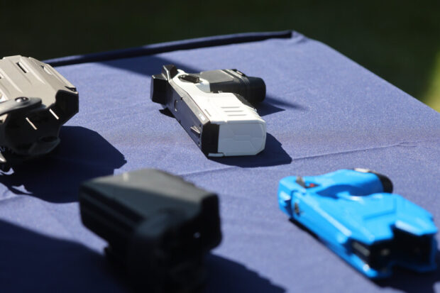 Dos pistolas taser, una blanca y otra azul, encima de una mesa con mantel azul marino.