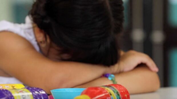 Niña descansa la cabeza en sus brazos.