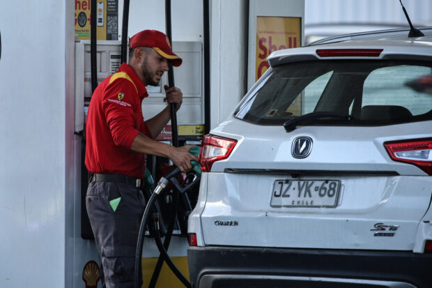 Un trabajador de la Shell se ve sosteniendo la manguera de combustible mientras carga bencina a un vehículo.