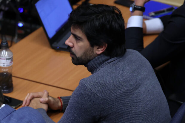 Joaquín Lavín León se ve de perfil sentado en una mesa de madera clara mientra ve al frente.