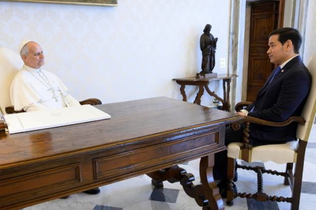 Papa León XIV y Marco Rubio, conversan sentados frente a frente y separados por una mesa de madera.