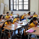 Alumnas sentadas en sus pupitres en un salón de clases. Todas visten ropa deportiva y polera amarilla.