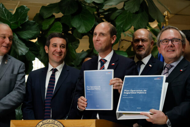 Autoridades del gobierno de Chile presentan el documento oficial del "Plan Operativo de Seguridad Pública" impreso en carpetas azules, durante un punto de prensa institucional.