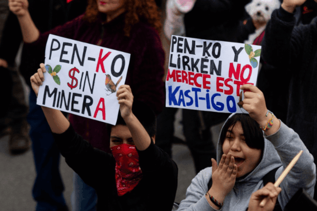Manifestantes sostienen carteles hechos a mano que dicen "Pen-ko sin minera" y "Pen-ko y Lirkén no merece este kast-igo" durante una protesta ambiental.