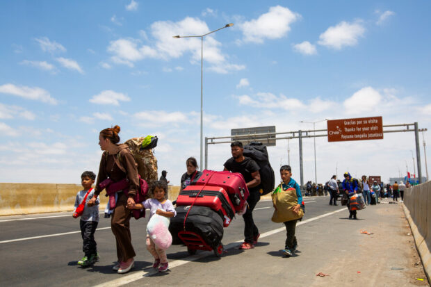 Familia de migrantes en la frontera Chile-Perú. Los padres llevan grandes maletas y sostienen a sus hijos pequeños de la manos.