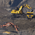 Maquinaria pesada trabajando en una mina a cielo abierto, mostrando una excavadora Komatsu amarilla cargando tierra en un camión minero de alto tonelaje, con otra excavadora Hitachi naranja en primer plano.