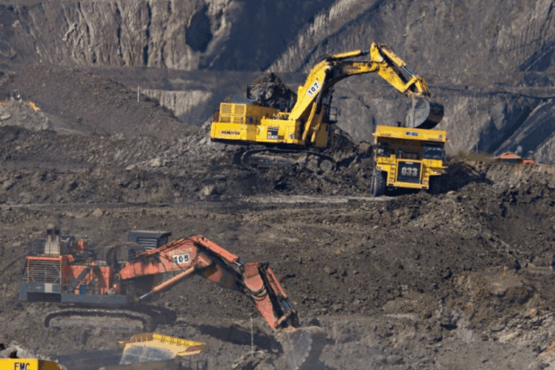 Maquinaria pesada trabajando en una mina a cielo abierto, mostrando una excavadora Komatsu amarilla cargando tierra en un camión minero de alto tonelaje, con otra excavadora Hitachi naranja en primer plano.
